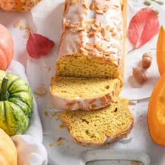 Bizcocho de calabaza Thermomix cubierto de glaseado y almendras. Rodeado de calabazas, hojas de otoño y bellotas.