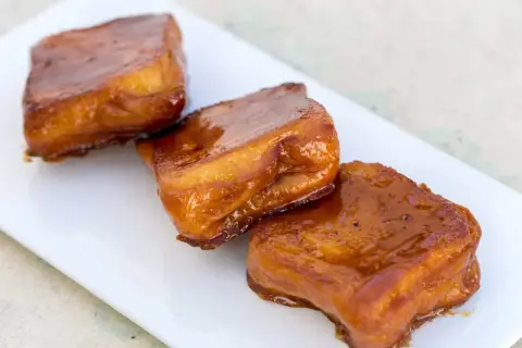 Tres torrijas de miel, doradas y brillantes, servidas en un plato blanco.