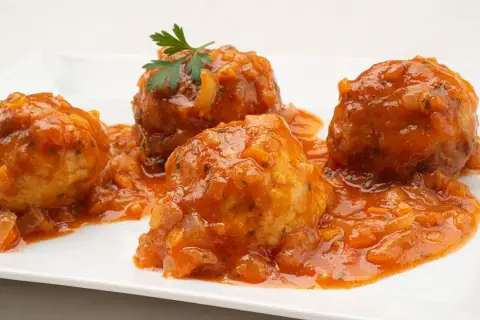 Cuatro albóndigas de rape en una salsa de tomate casera, decoradas con perejil fresco.