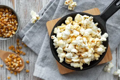 Palomitas recién hechas en sartén, listas para disfrutar. Maíz de palomitas en un cuenco y cuchara de madera.