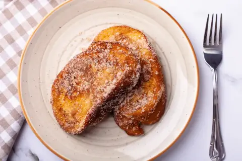 Dos torrijas doradas y azucaradas en un plato, listas para disfrutar. ¡Perfectas si las haces en Thermomix!