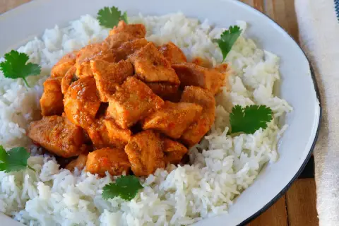 Sabroso pollo tikka masala servido sobre una cama de arroz blanco, decorado con hojas de cilantro fresco.