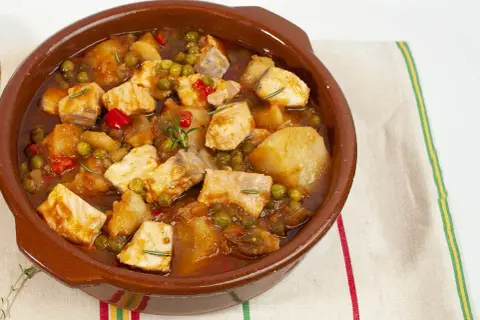 Un apetitoso marmitako de salmón, con trozos de pescado, patatas, guisantes y pimientos rojos, servido en cazuela de barro.