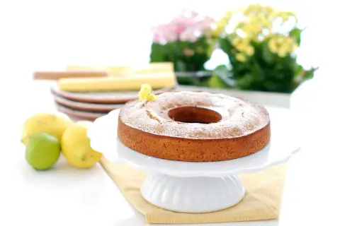 Bizcocho de limón Thermomix esponjoso y dorado, espolvoreado con azúcar glas. Limones y lima frescos al lado.