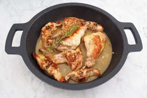 Sabroso conejo al ajillo en una sartén, con trozos dorados de carne, ajo picado y una ramita de romero fresco.