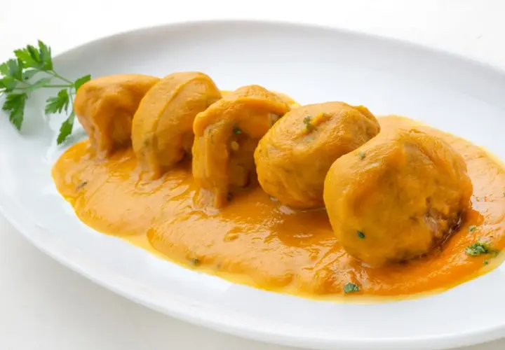 Cinco albóndigas en salsa arguiñano, servidas en un plato blanco con perejil fresco.