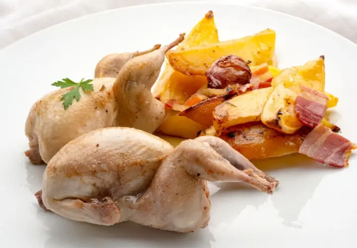 Dos codornices al horno, doradas y jugosas, acompañadas de patatas rústicas asadas con tocino y hierbas.