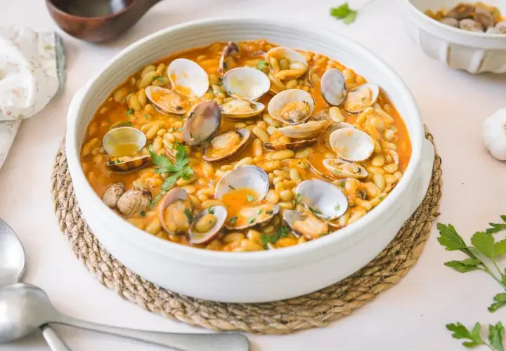 Plato de verdinas con almejas en salsa, decorado con perejil fresco. Un festín marinero y vegetal.
