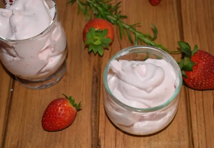 Delicioso postre con fresas, cremoso y ligero, servido en copas. Fresas frescas y romero decoran la mesa de madera.