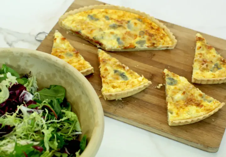 Un delicioso pastel de puerros recién horneado, cortado en porciones, junto a una ensalada fresca en un cuenco de madera.