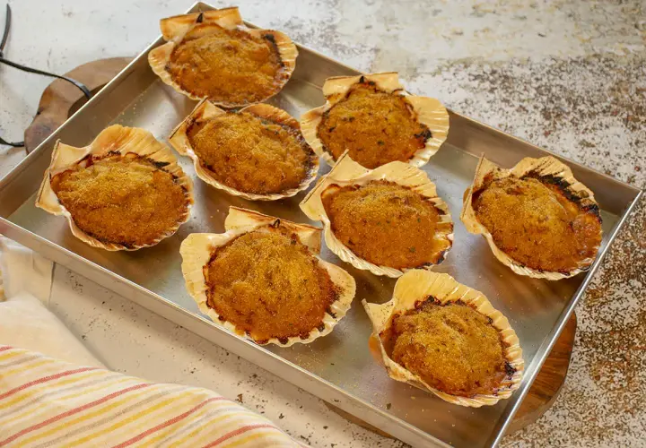 Ocho vieiras a la gallega gratinadas en sus conchas, listas para disfrutar.