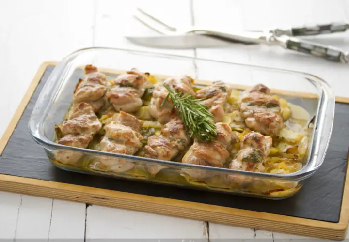 Contramuslos de pollo al horno crujientes, dorados y jugosos, servidos en una fuente de cristal con patatas y romero.
