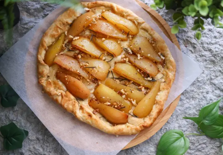 Deliciosa tarta de pera rústica, con trozos de pera caramelizada, nueces y romero, sobre una base dorada y crujiente.