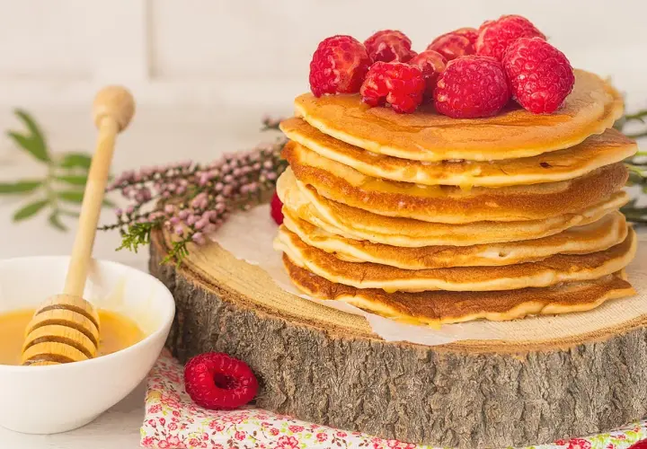Una pila de tortitas de avena doradas, cubiertas con frambuesas frescas y miel, listas para disfrutar.