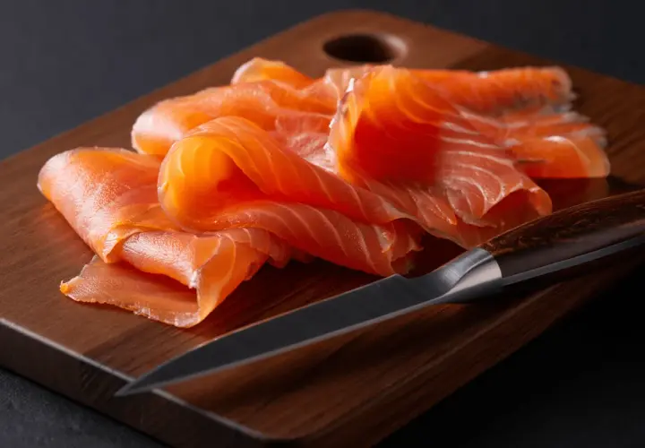 Finas lonchas de salmón ahumado sobre tabla de madera. Se puede congelar el salmón ahumado para conservarlo fresco.