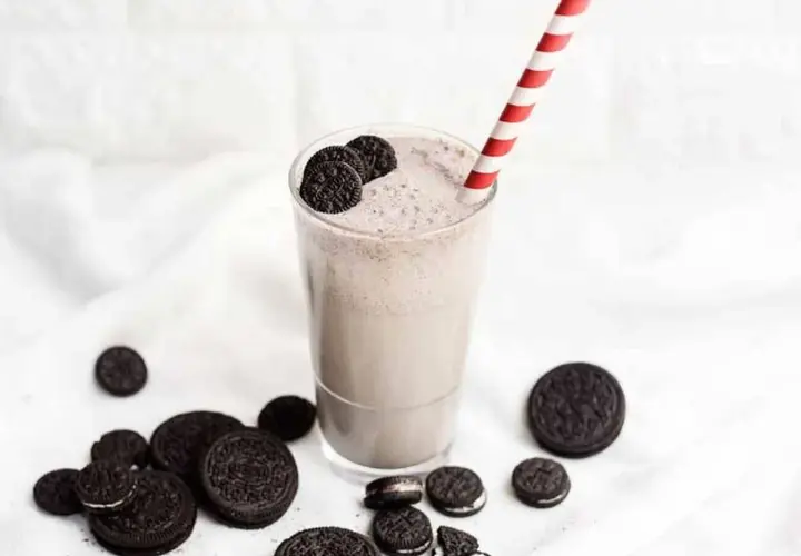Delicioso batido de oreo cremoso, adornado con galletas enteras y trozos, listo para disfrutar con su pajita a rayas.