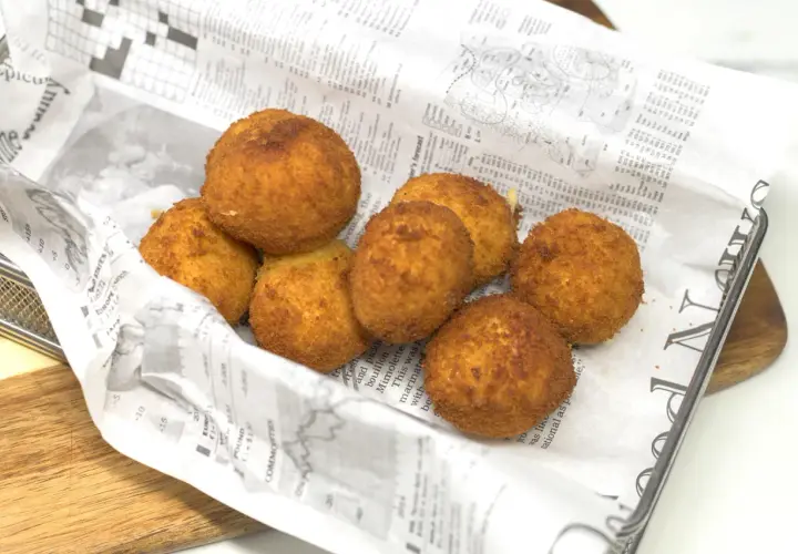 Croquetas de gambas doradas y crujientes, servidas sobre papel de periódico en una cesta metálica.