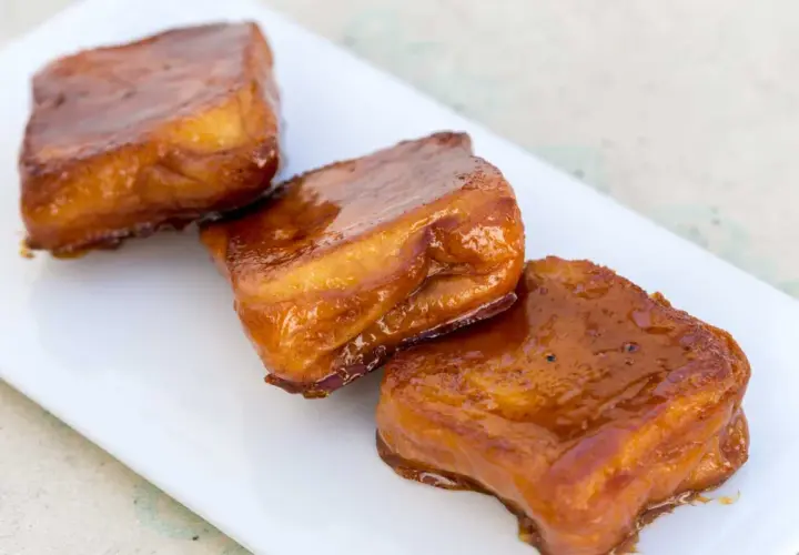 Tres torrijas de miel, doradas y brillantes, servidas en un plato blanco.