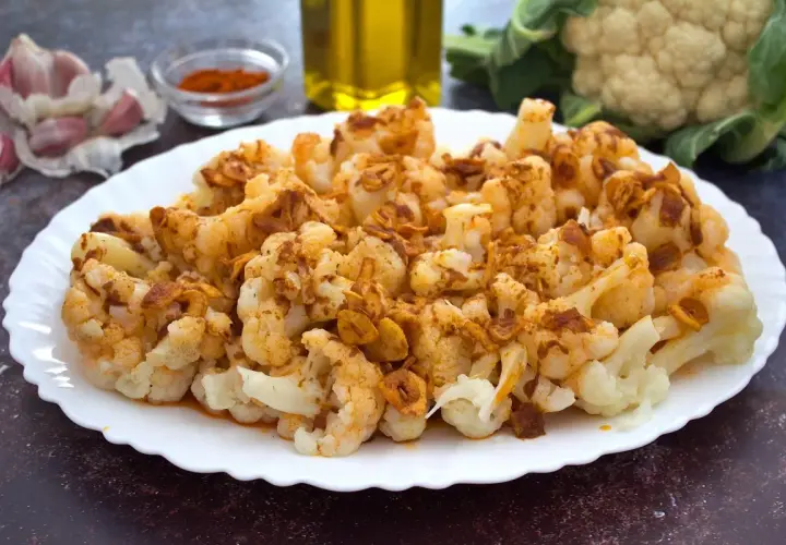 Coliflor al ajoarriero, con trozos dorados de ajo y pimentón, servida en un plato blanco.