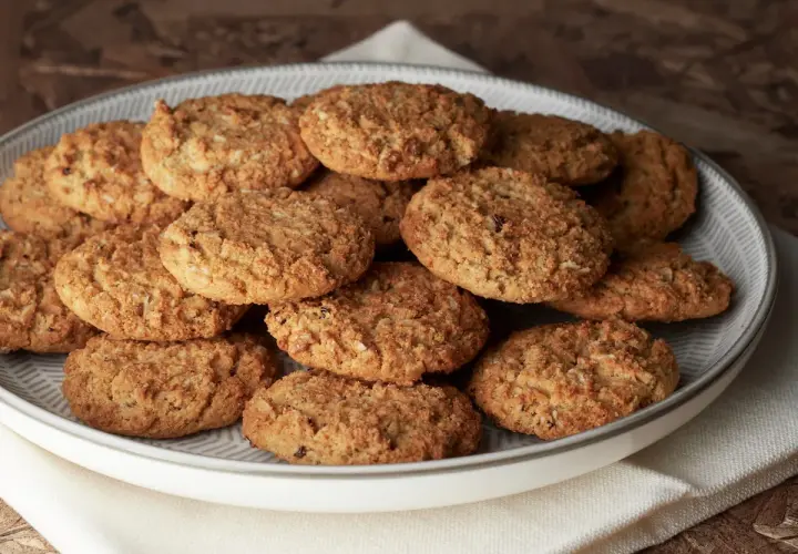 Montón de carajitos del profesor, galletas doradas y crujientes con avena y coco, apiladas en un plato gris.