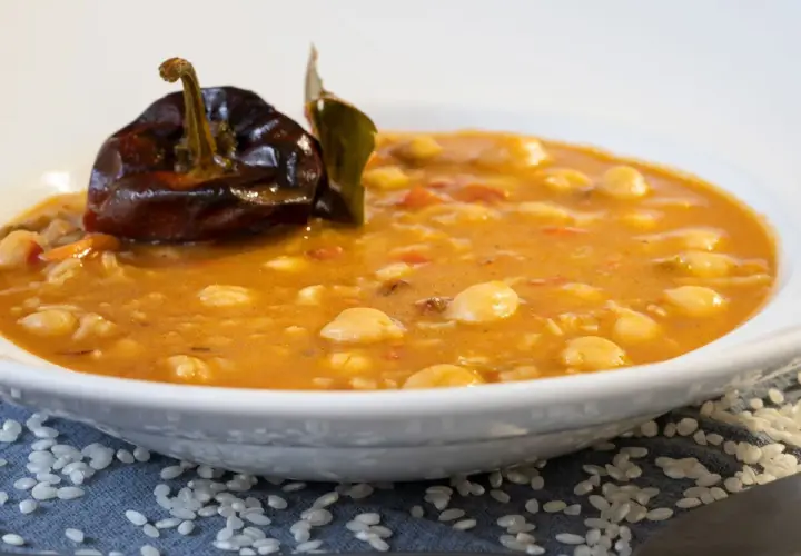 Un plato de garbanzos con arroz, reconfortante y sabroso, coronado con un pimiento seco y una hoja de laurel.