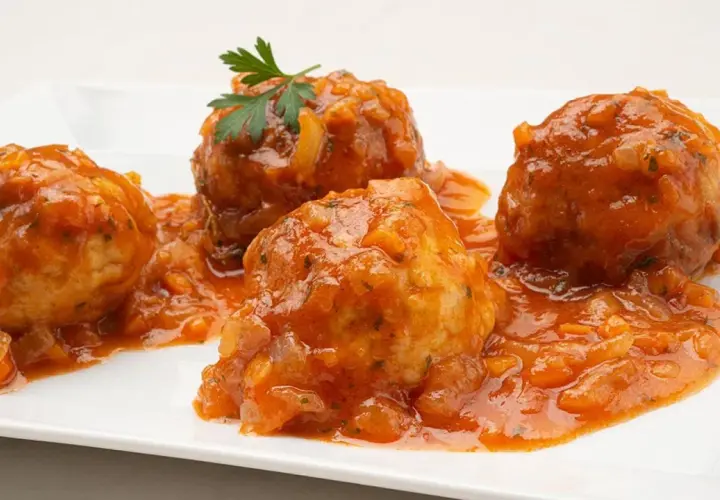 Cuatro albóndigas de rape en una salsa de tomate casera, decoradas con perejil fresco.