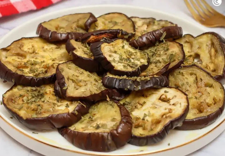 Rodajas de berenjenas al horno, doradas y espolvoreadas con hierbas aromáticas, listas para disfrutar.