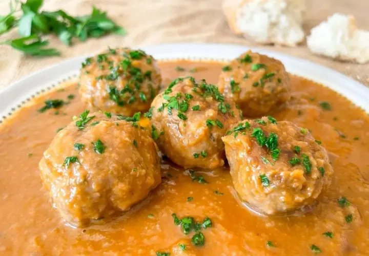 Cinco deliciosas albóndigas al horno en una rica salsa, espolvoreadas con perejil fresco. ¡Perfectas para mojar pan!