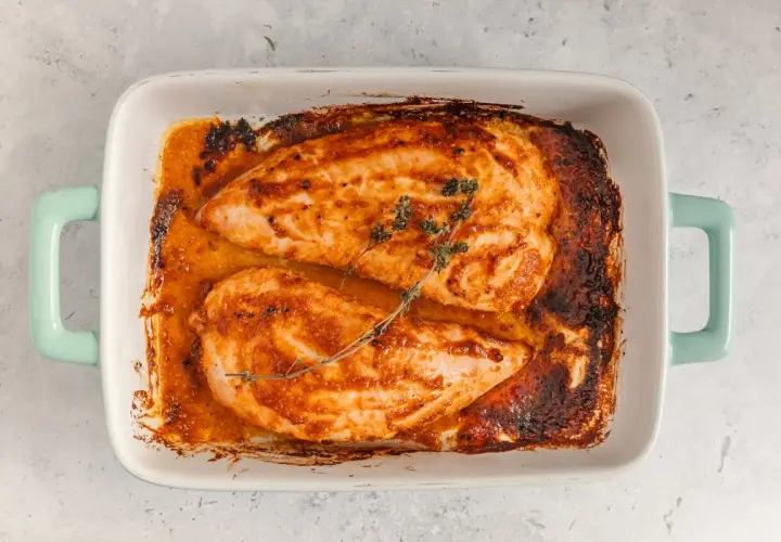 Dos jugosos solomillos de pavo al horno, dorados y con hierbas, reposan en una fuente blanca con asas turquesa.