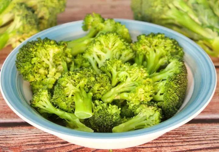 Brocoli al microondas en un cuenco azul sobre madera.