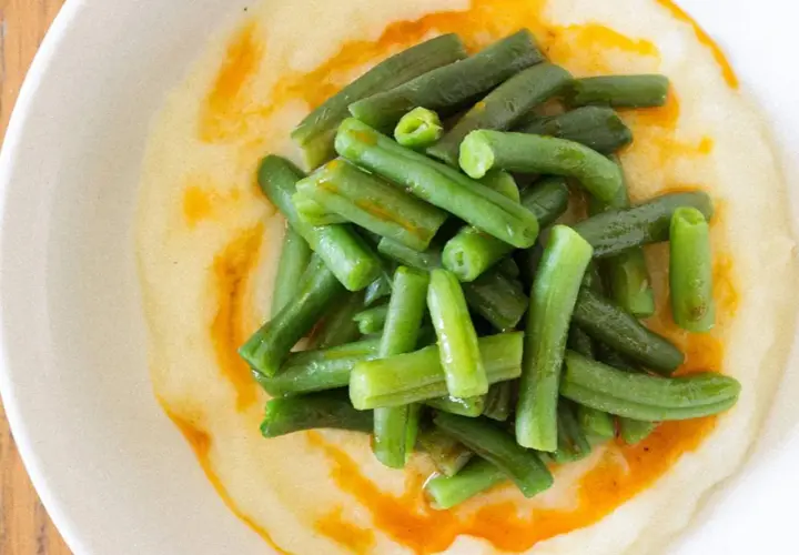 Judías verdes frescas y tiernas sobre una cremosa base de puré de patatas, con un toque de aceite de pimentón.