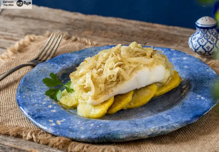 Delicioso bacalao a la portuguesa, servido sobre patatas y cubierto con cebolla caramelizada.