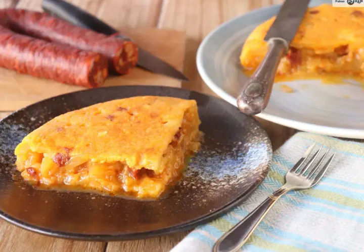 Deliciosa tortilla de chorizo, jugosa y dorada, servida en plato oscuro. Chorizos crudos al fondo.