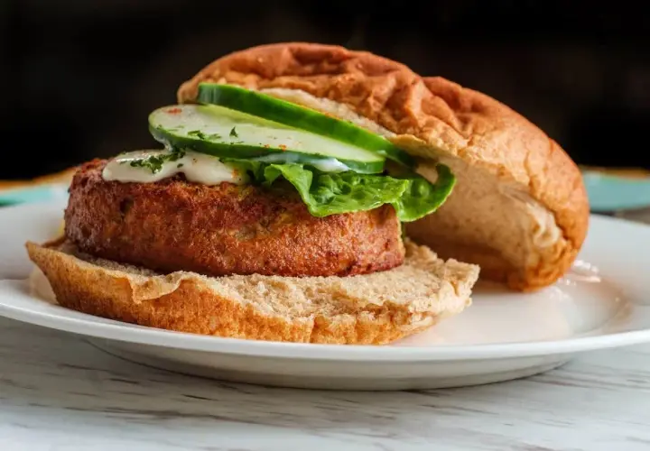 Deliciosa hamburguesa de salmón con lechuga, pepino y salsa cremosa en un pan tostado.