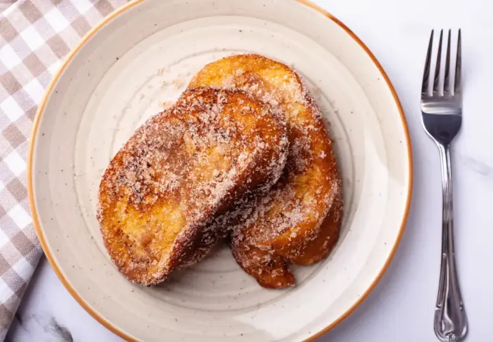 Dos torrijas doradas y azucaradas en un plato, listas para disfrutar. ¡Perfectas si las haces en Thermomix!