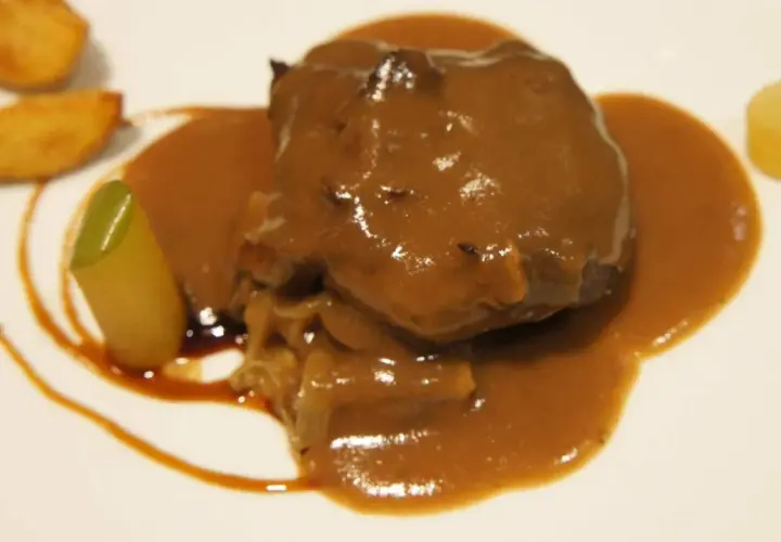 Carrilleras de ternera estofadas en salsa, acompañadas de patatas y un toque verde.