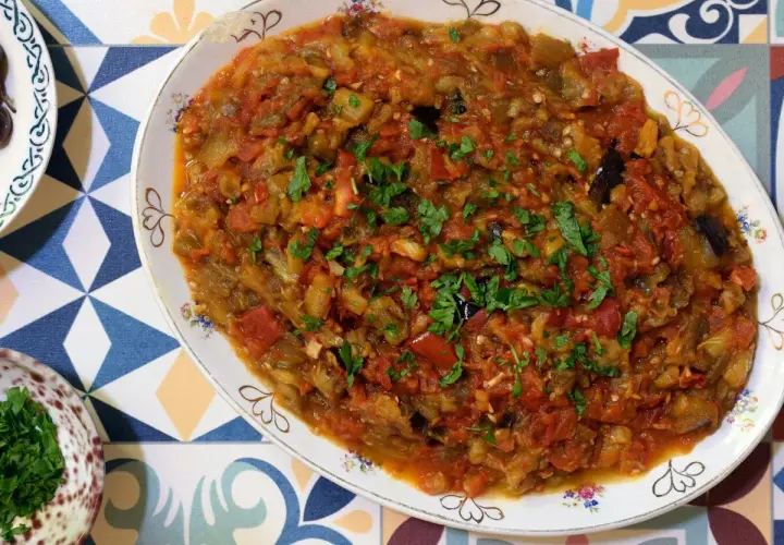 Un plato de pisto con berenjena, lleno de verduras cocidas y espolvoreado con perejil fresco.