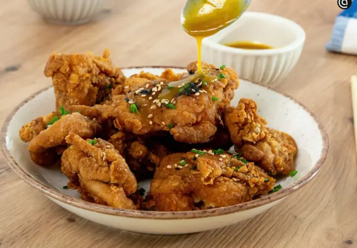 Crujiente pollo frito coreano bañado en salsa dorada, espolvoreado con semillas de sésamo y cebollín. ¡Un bocado irresistible!