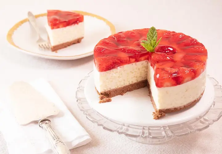 Deliciosa tarta de fresa con una capa cremosa y cobertura de gelatina de fresa, decorada con menta. Una porción ya servida en un plato.