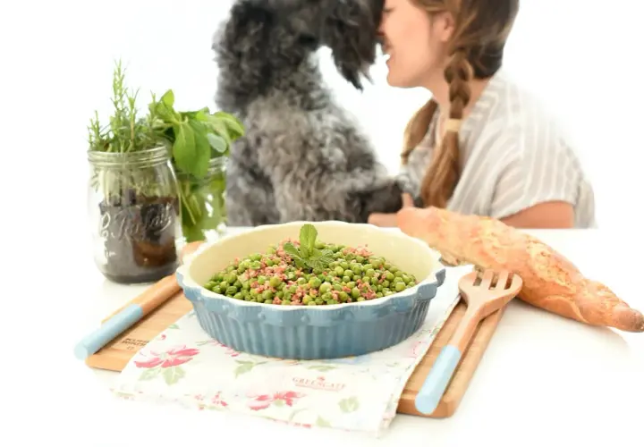 Guisantes con jamón, un plato sencillo y delicioso preparado en Thermomix. Una mujer y su perro disfrutan de la comida.