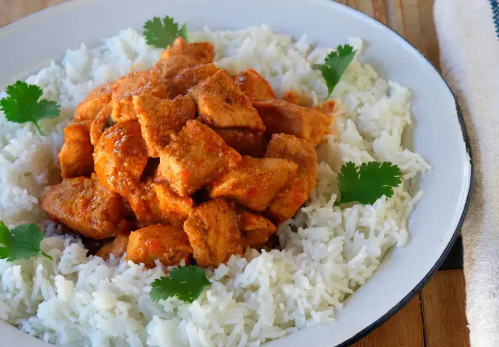 Sabroso pollo tikka masala servido sobre una cama de arroz blanco, decorado con hojas de cilantro fresco.