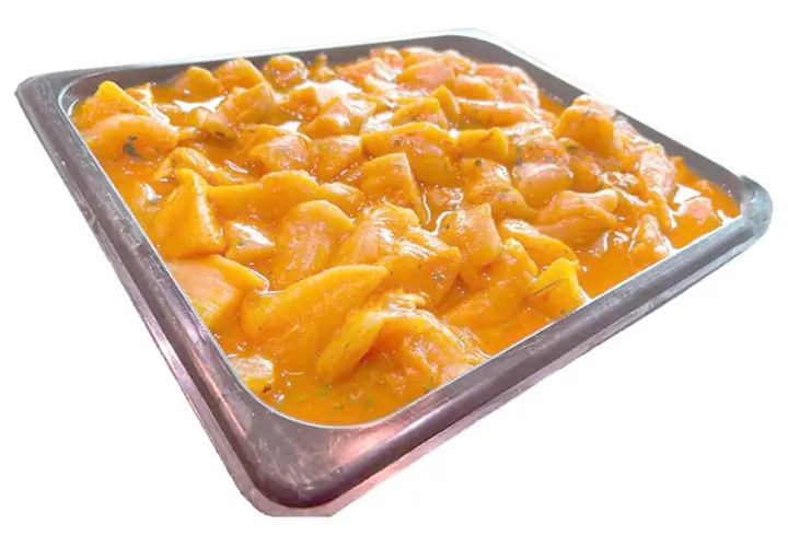 Bandeja metálica llena de trozos de pollo marinados en una salsa anaranjada, listos para convertirse en deliciosos pinchitos.