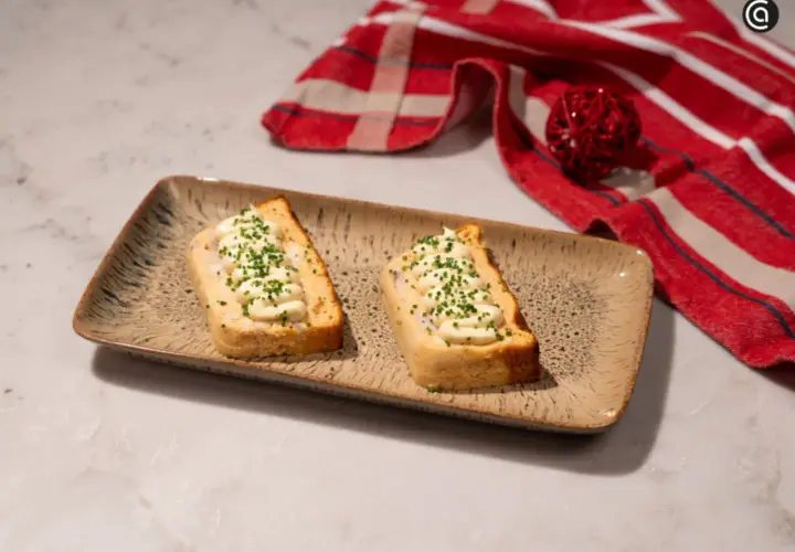 Dos porciones de pastel de cabracho, cubiertas con mayonesa y cebollino, servidas en una bandeja rústica.