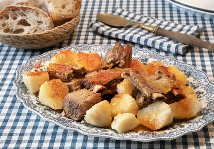 Un plato de carne o caldeiro con patatas cocidas y pan rústico en una cesta.