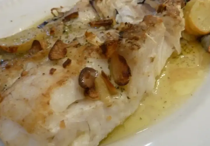 Merluza al horno sin patatas, jugosa y dorada, con láminas de ajo crujientes y hierbas aromáticas. Un plato ligero y sabroso.