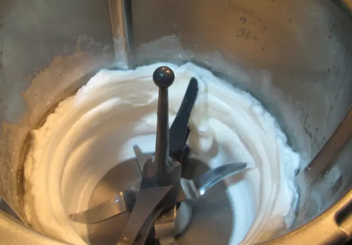 Montar claras a punto de nieve en Thermomix. La mezcla cremosa y blanca rodea las cuchillas.