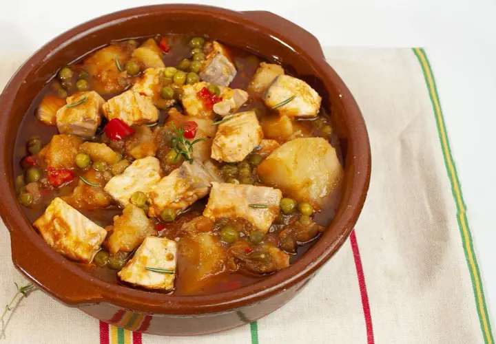 Un apetitoso marmitako de salmón, con trozos de pescado, patatas, guisantes y pimientos rojos, servido en cazuela de barro.
