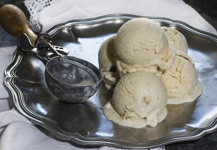 Cremoso helado de plátano derritiéndose en una bandeja de plata, junto a un cucharón.