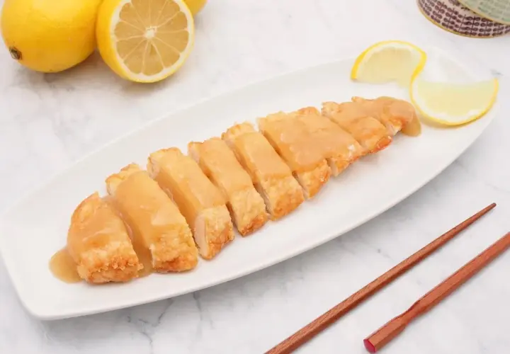 Pollo al limón chino servido en una bandeja blanca, con limones frescos y palillos de madera.