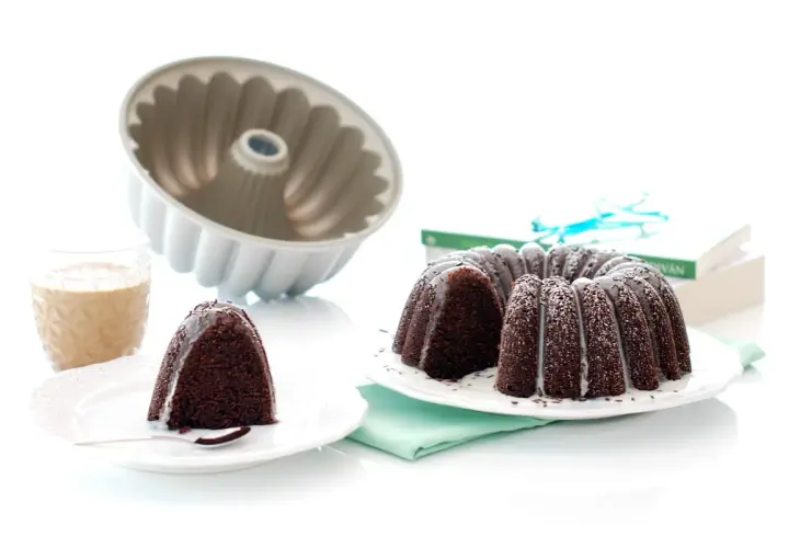 Bizcocho chocolate Thermomix, recién horneado y decorado con glaseado blanco. Un trozo ya servido con un vaso de leche.